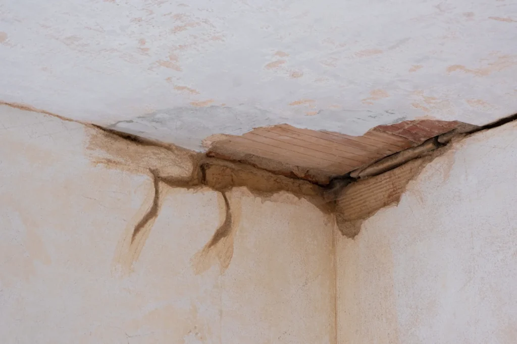 A damaged corner of a ceiling and wall shows peeling plaster, exposed wooden slats, and dark water stains—clear signs that a professional water damage restoration service in Lyndhurst is needed to address the deterioration.